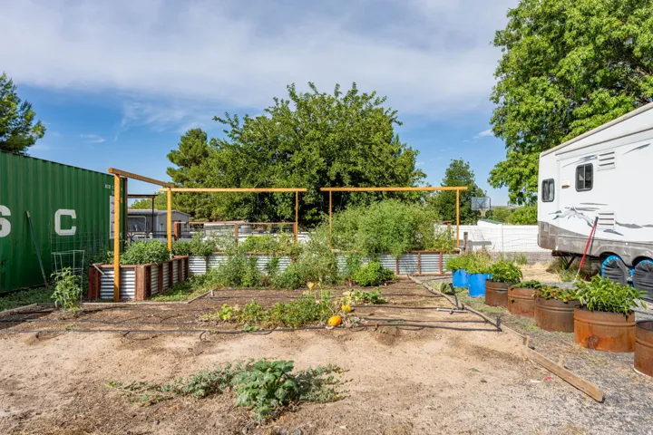 Productive garden space featuring raised planting beds, sturdy wood-frame pergola structure, mature shade trees, and direct access to RV parking with utility connections visible on the property