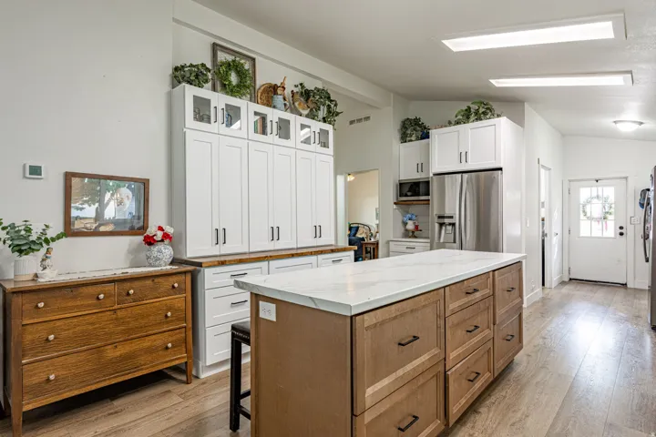 Chef's kitchen featuring a two-tier island with wood-finish cabinetry and white quartz countertops, stainless steel refrigerator and built-in appliances, white shaker-style upper cabinetry with open shelving, wood-finish flooring, and abundant natural lig