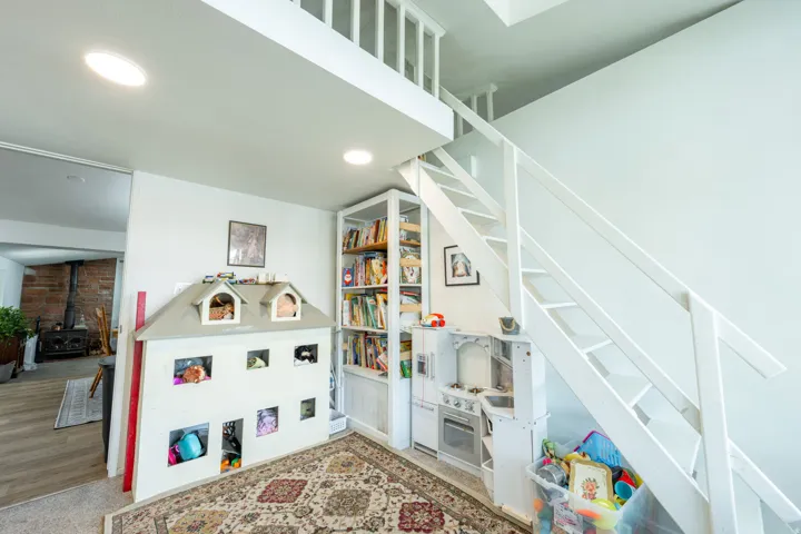 Bright, open loft-style space featuring white shiplap staircase with integrated storage, built-in shelving throughout, recessed ceiling lighting, and wood-finish flooring