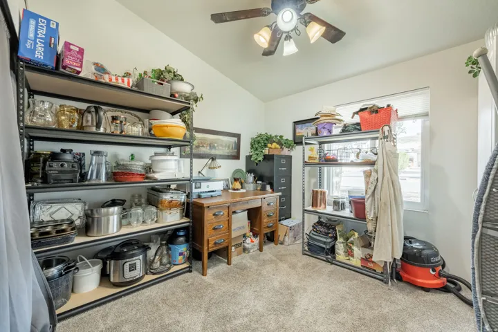 Versatile storage room featuring industrial-style metal shelving units, wood-finish cabinetry, carpeted flooring, and ceiling fan with integrated lighting