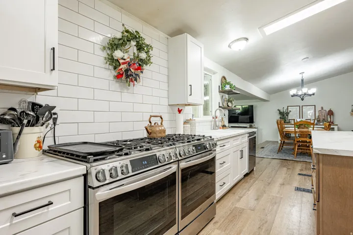 Chef's kitchen featuring stainless steel dual-fuel range with professional-grade cooktop, white subway tile backsplash, white cabinetry with black hardware, quartz countertops, and wood-finish flooring throughout the open layout