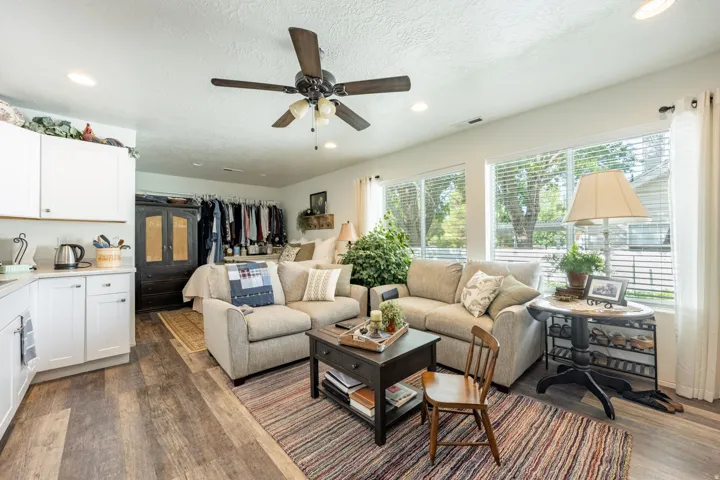 Open-concept living area featuring a beige upholstered sectional, wood-finish flooring, and abundant natural light from multiple large windows
