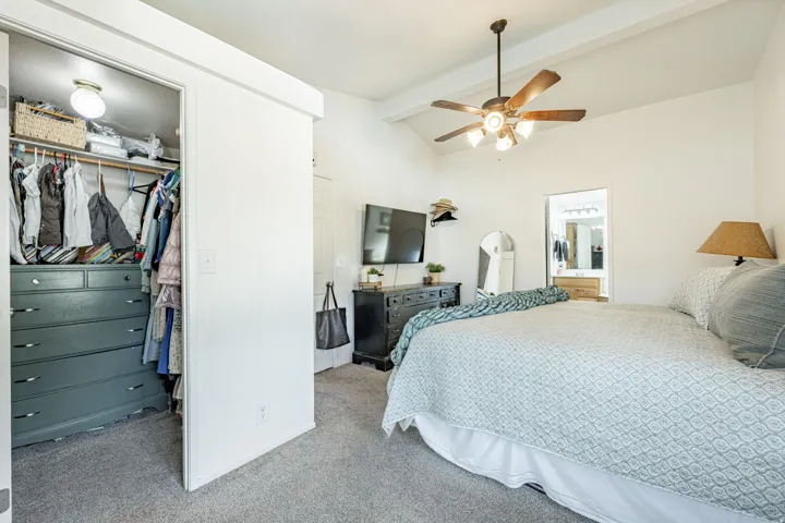 Vaulted ceiling with exposed beams, ceiling fan with integrated lighting, carpeted flooring, built-in closet, and a light-filled interior