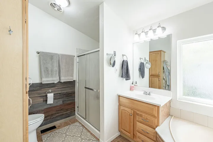 Spa-inspired primary bathroom featuring a wood-finish vanity with dual drawers, white ceramic sink, and polished chrome fixtures