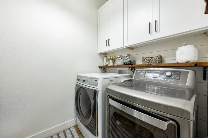 Laundry area featuring white cabinetry with dark pulls, a wood-finish shelf, and shiplap wall paneling