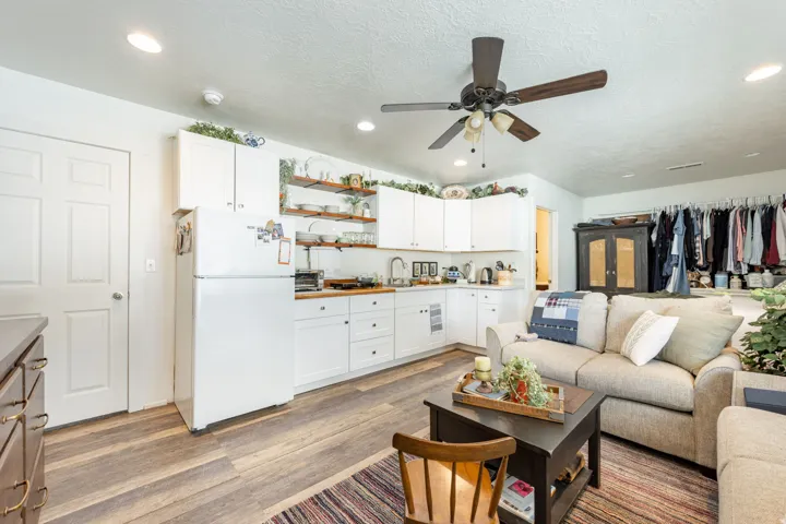 Open-concept living space featuring white cabinetry with wood-finish shelving, stainless steel appliances, wood-finish flooring throughout, and a ceiling fan with recessed lighting