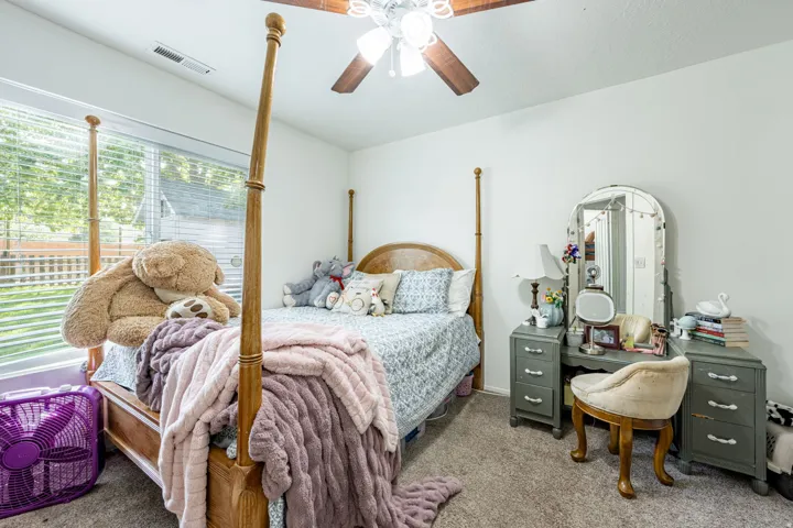 Charming bedroom featuring a four-poster wood bed frame, carpet flooring, and abundant natural light from large windows