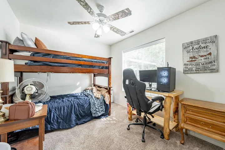 Bedroom featuring a wooden loft bed with storage shelving, carpeted flooring, ceiling fan with light fixture, and a dedicated workspace with desk and chair