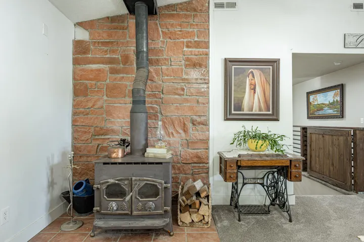 Rustic brick fireplace with cast-iron wood stove and integrated wood storage, complemented by wood-finish flooring and exposed brick detailing