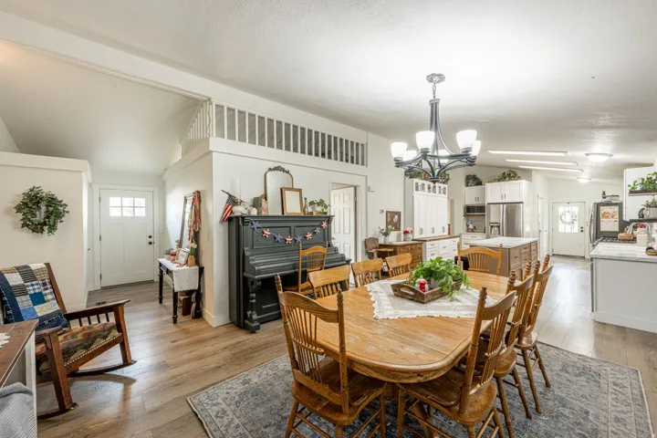 Open-concept dining and kitchen area featuring hardwood flooring, a wood-finish dining table with seating for six, stainless steel appliances, white cabinetry, and a multi-light chandelier