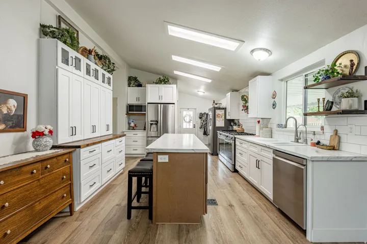 Chef's kitchen featuring white cabinetry with stainless steel appliances, a large center island with wood-finish base, white subway tile backsplash, quartz countertops, recessed and pendant lighting, wood-finish flooring, and abundant storage with open sh