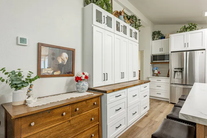 White shaker-style cabinetry with black hardware, wood-finish flooring, and stainless steel appliances