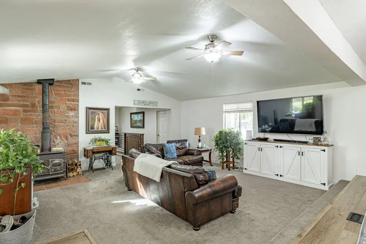 Vaulted ceilings with recessed lighting, brick-clad wood-burning stove, carpet flooring, and a white media console with barn door-style fronts