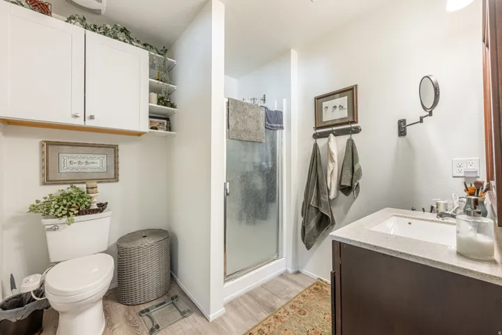 White cabinetry, an enclosed shower, a single vanity with an integrated sink, and wood-finish flooring