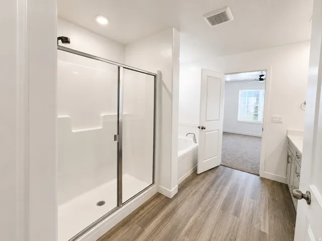 Walk-in shower with sliding glass door, soaker tub, dual vanity with undermount sinks, and wood-finish flooring