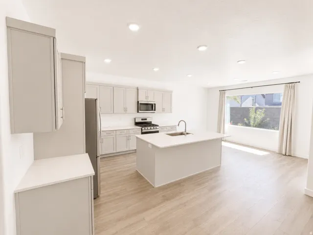 Kitchen featuring light-toned cabinetry, stainless steel appliances, a center island with sink, and wood-finish flooring