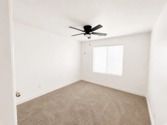 Neutral tone paint throughout, carpet flooring, a window with horizontal blinds, and a ceiling fan with integrated lighting