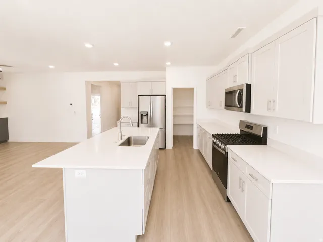 Modern kitchen featuring an expansive island with an undermount sink, light wood-finish flooring, white cabinetry, and stainless steel appliances