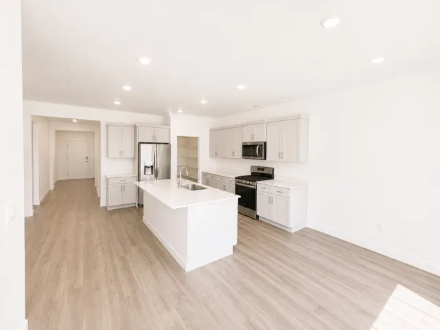 Open-concept kitchen featuring light-toned cabinetry, stainless steel appliances, a center island with a sink, and wood-finish flooring throughout