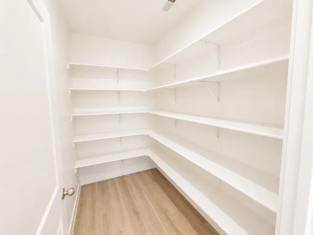 Expansive pantry featuring ample built-in shelving, light wood-finish flooring, and white painted walls