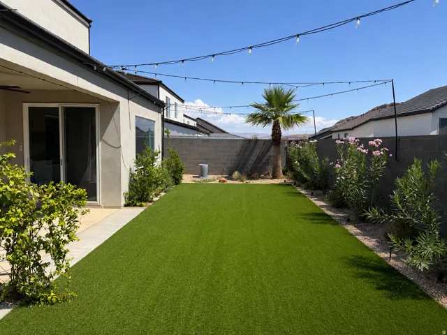 Spacious backyard featuring artificial turf, string lighting, established plantings, and a privacy wall