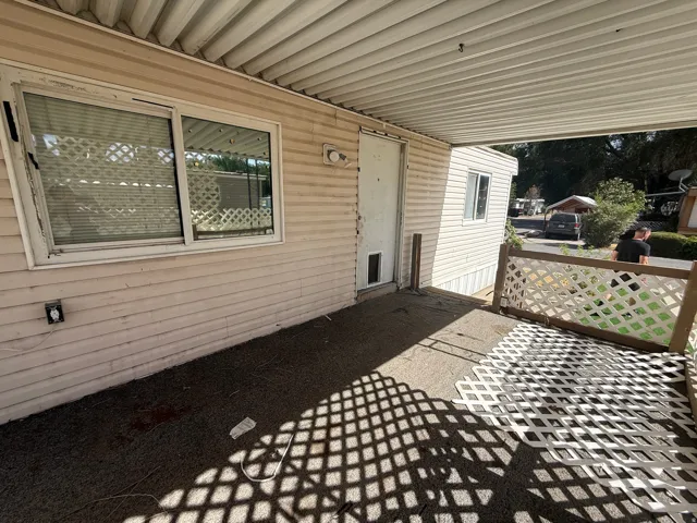 Covered outdoor patio area featuring a lattice railing, exterior siding, and a sliding window