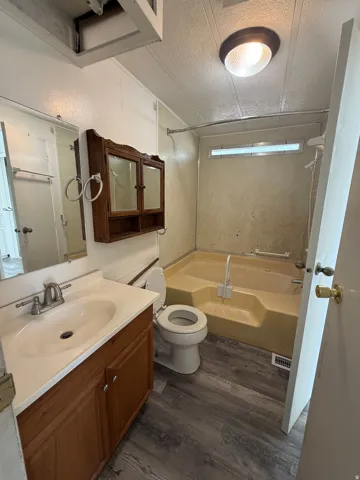 Bathroom featuring a wood-finish vanity with an integrated sink, a built-in medicine cabinet, a full-size bathtub, and wood-finish flooring