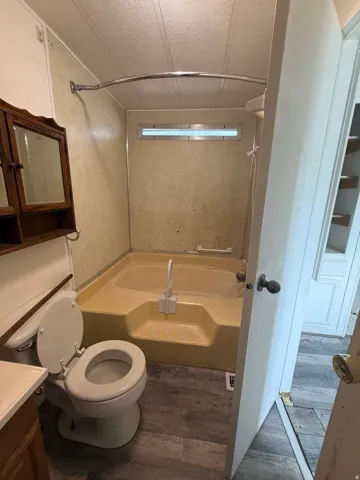 Step-up bathtub with shower surround, wood-finish flooring, and wall-mounted storage cabinet
