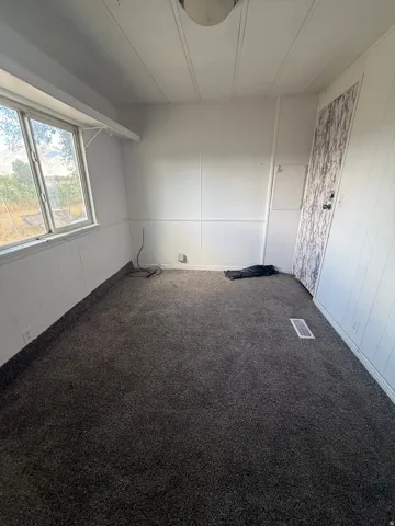Window with outdoor scenery, wall-to-wall carpeting, paneled walls, ceiling-mounted light fixture, and a solid-panel door
