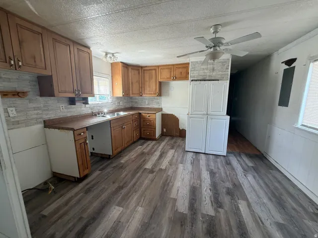 Wood-finish flooring throughout, wood cabinetry, dual basin sink, ceiling fan, and white paneled walls