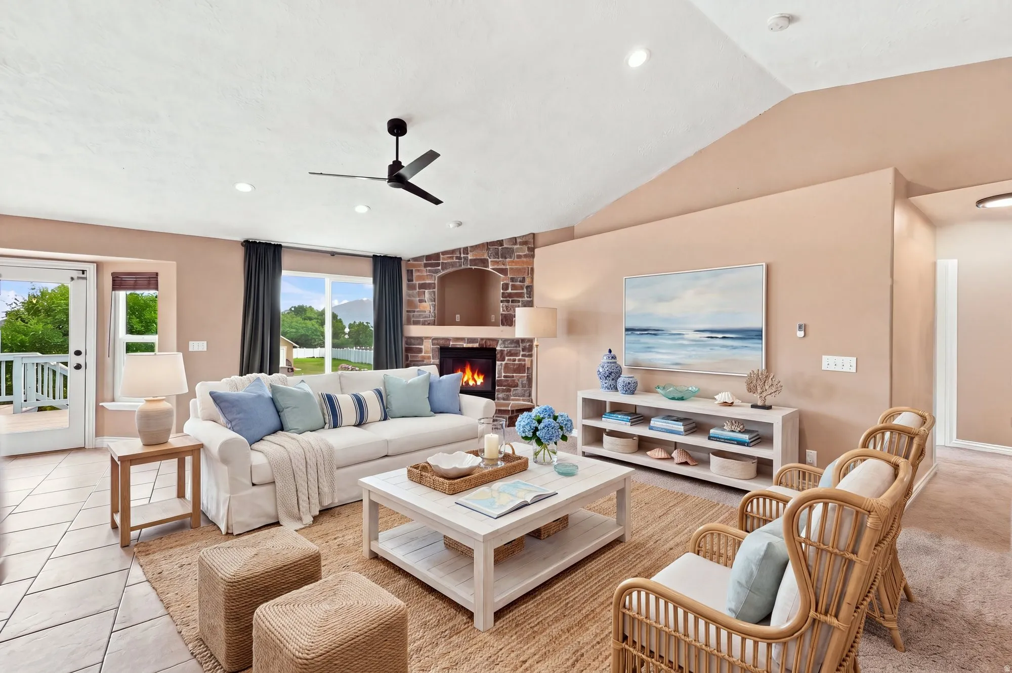 Vaulted ceiling with recessed lighting, stone-clad fireplace, ceiling fan, large window with outdoor scenery, and tiled flooring