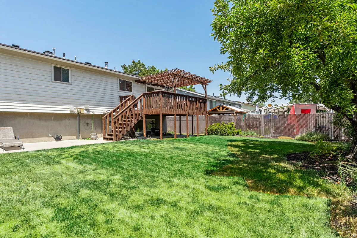 Expansive backyard oasis featuring a mature shade tree, lush manicured lawn, and a substantial wood-constructed deck with pergola overhead—ideal for outdoor entertaining and recreation