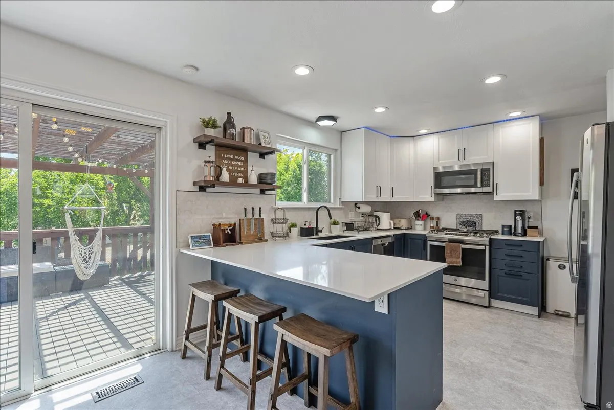 Kitchen featuring white upper cabinetry, contrasting blue lower cabinetry, stainless steel appliances, and a central island with a light-toned countertop