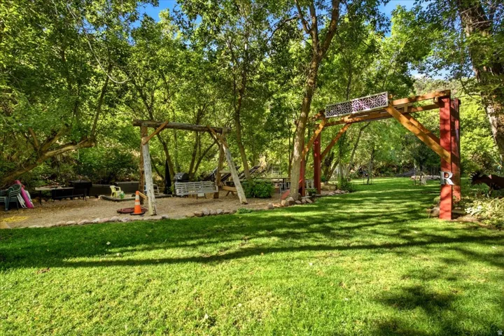 Manicured lawn, mature trees, wooden archway with decorative metalwork, and a built-in wooden swing set