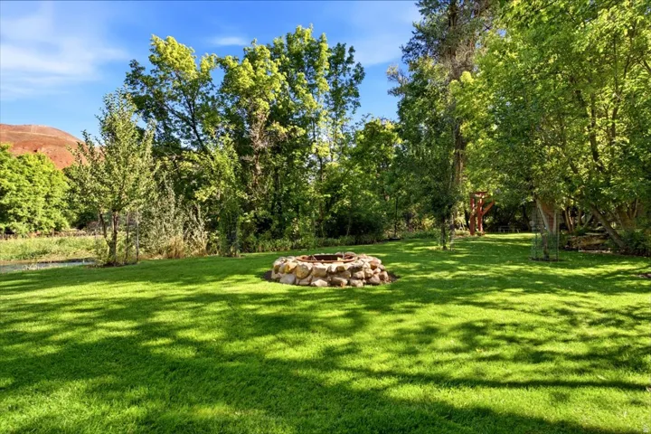 Expansive grounds featuring a manicured lawn with mature shade trees and natural stone fire pit, set against rolling hillside backdrop with established tree canopy providing year-round privacy and character