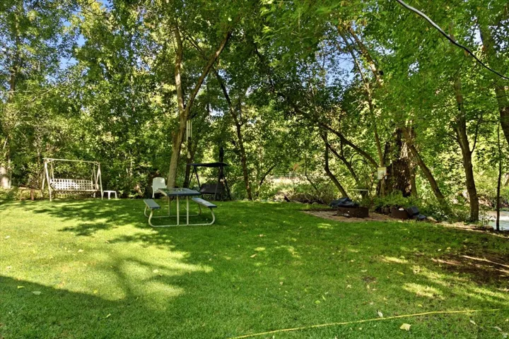 Expansive manicured lawn with mature trees, a designated fire pit area, and a natural water feature