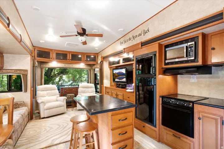 Built-in entertainment center, integrated kitchen appliances, central island with countertop, wood-finish cabinetry, and overhead ceiling fan