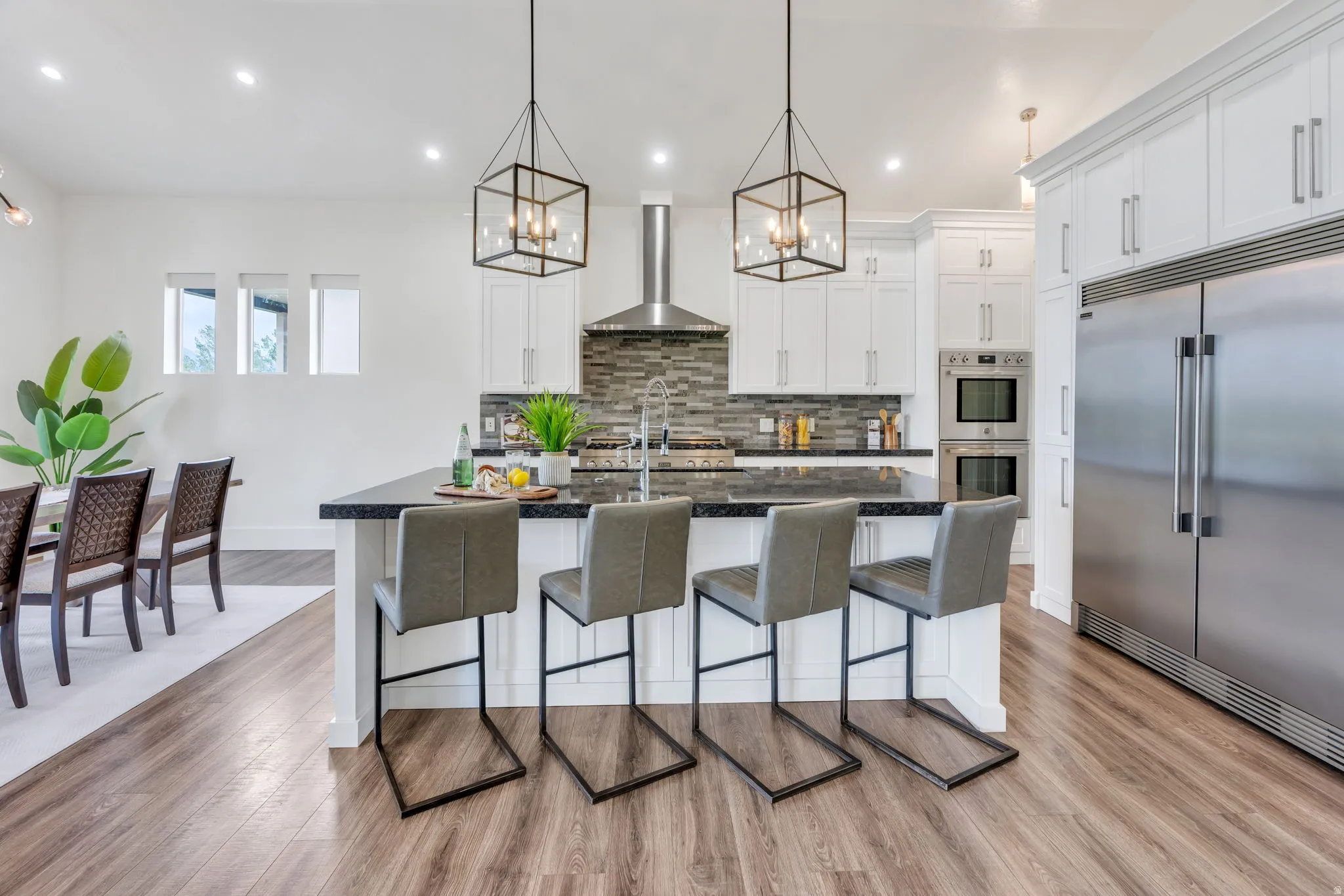 Gourmet kitchen with wood-finish flooring, white cabinetry, dark countertops, stainless steel appliances, and a tiled backsplash