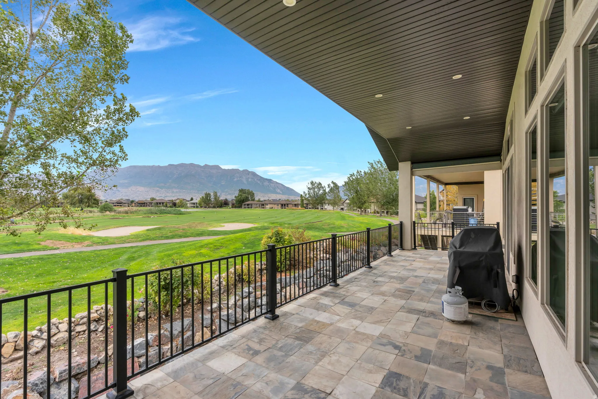 Spacious covered patio with stone-finish flooring, black metal railing, and recessed lighting