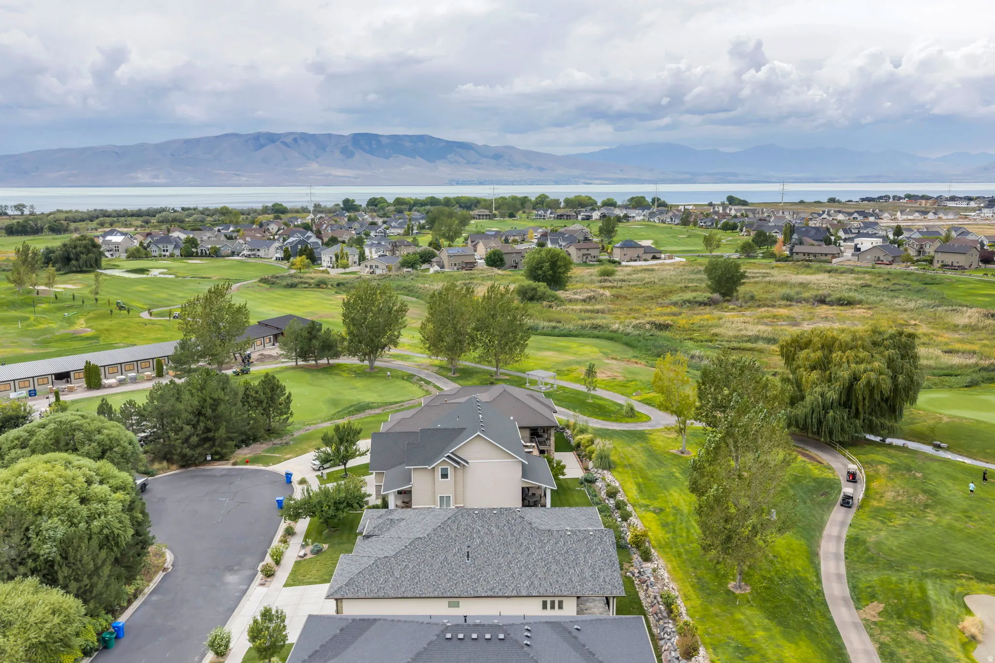 Aerial perspective showcasing residential properties, expansive green spaces, and distant body of water with mountains