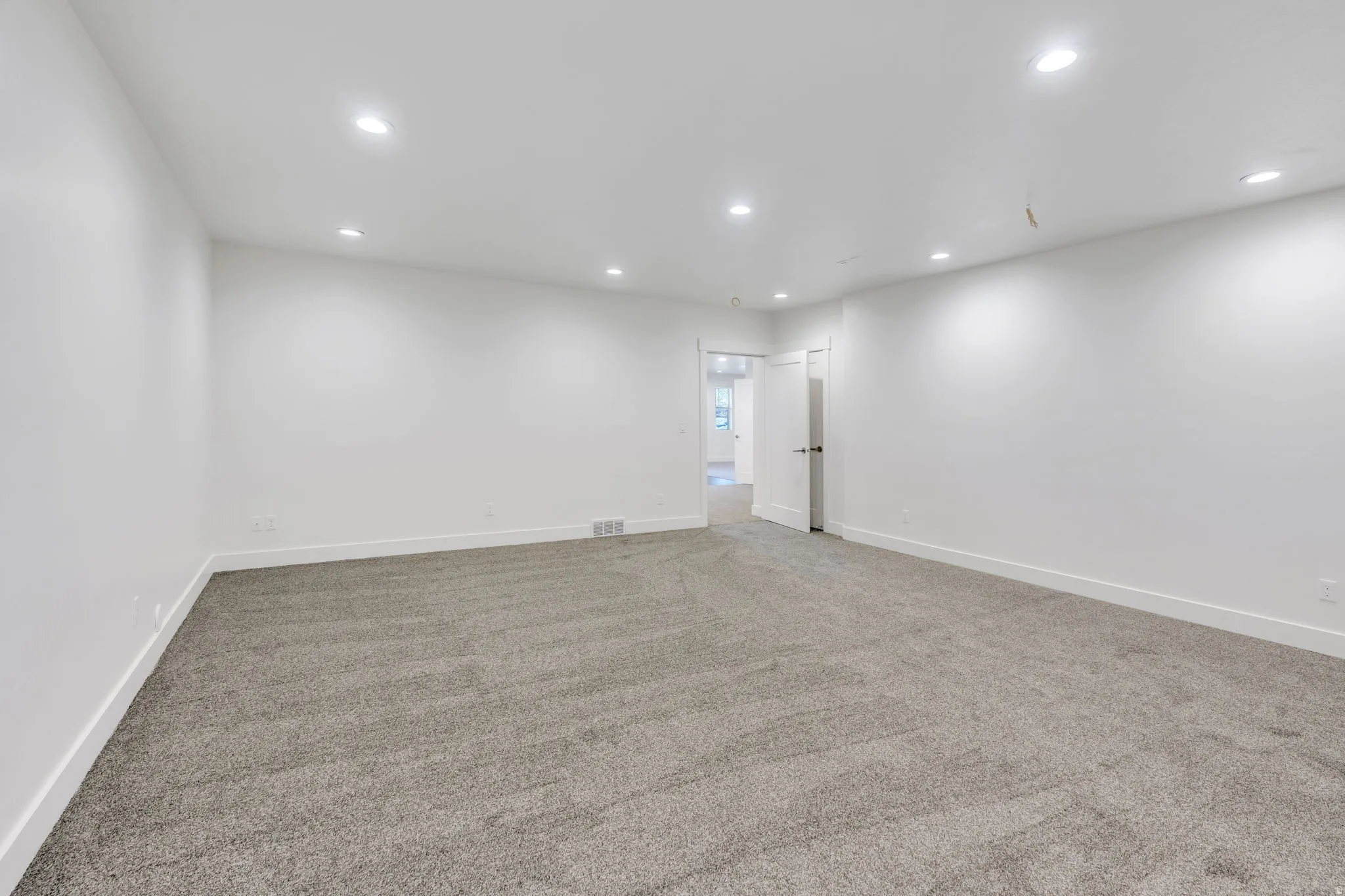 Spacious room featuring neutral carpeting, recessed lighting, and white painted walls