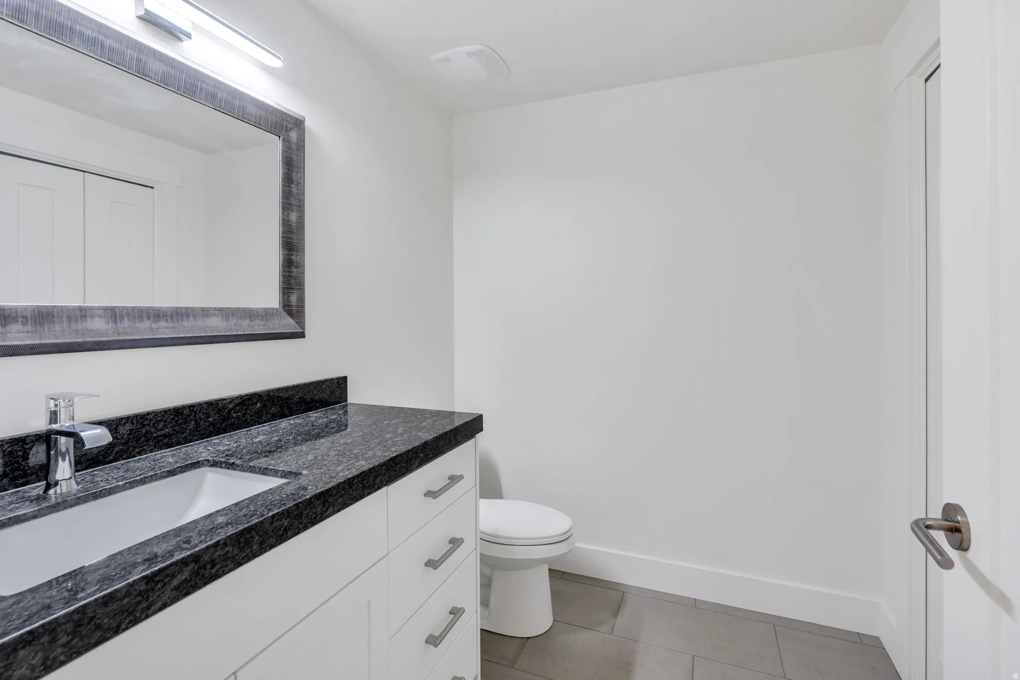 Modern bathroom featuring a floating vanity with dual sinks, polished stone countertop, and chrome fixtures
