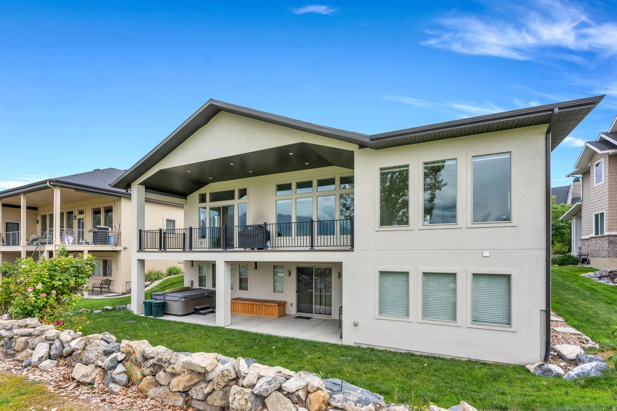 Modern stucco exterior with an angled roofline, upper-level balcony with black railing, lower-level covered patio, and expansive windows