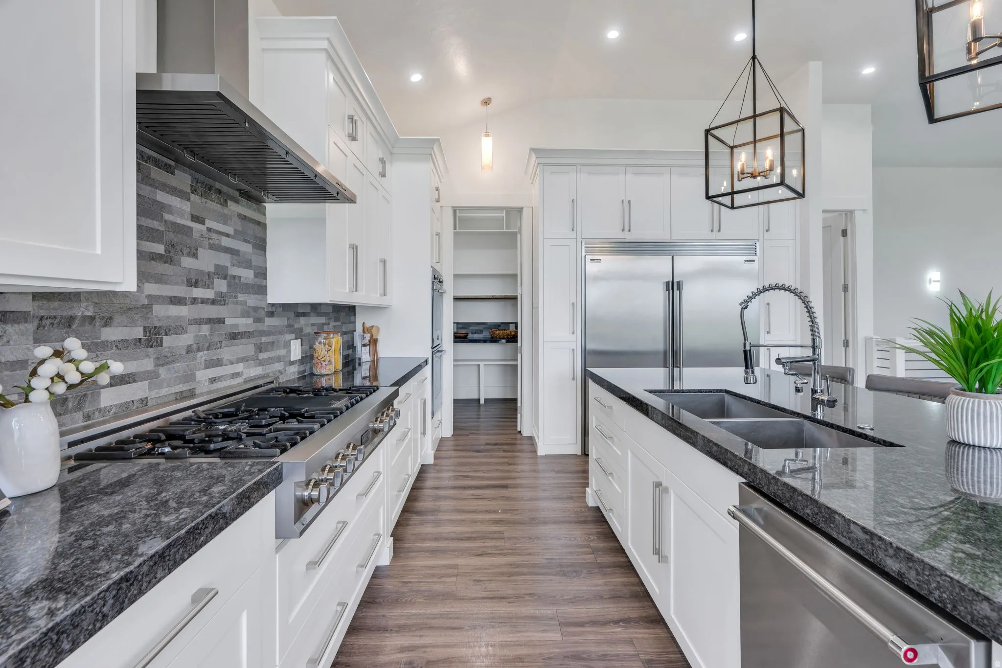 Well-appointed kitchen featuring white cabinetry, dark stone countertops, stainless steel appliances, and a tiled backsplash