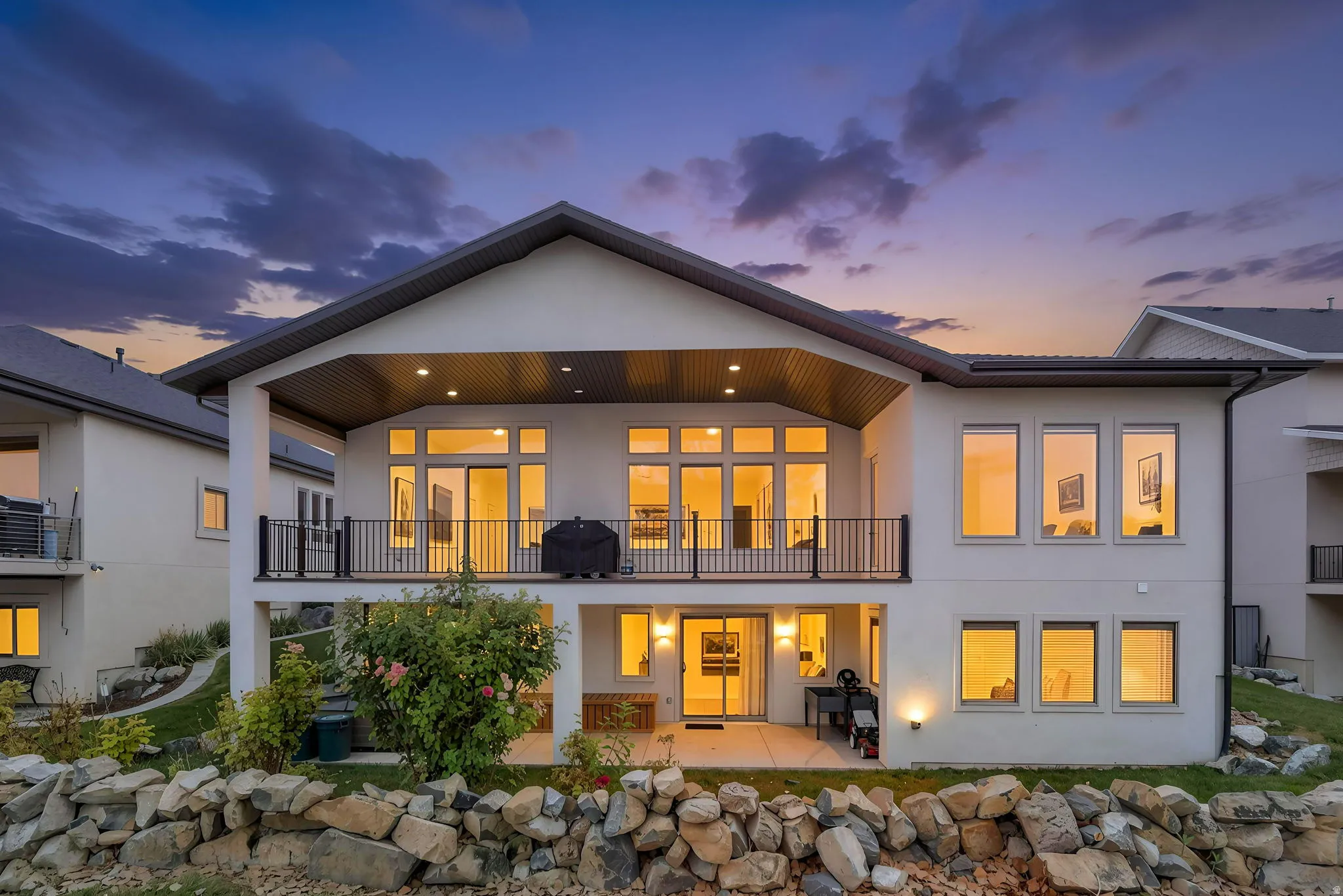 Multi-level property with an upper-level balcony featuring black iron railings, a covered patio on the lower level, and extensive large format windows