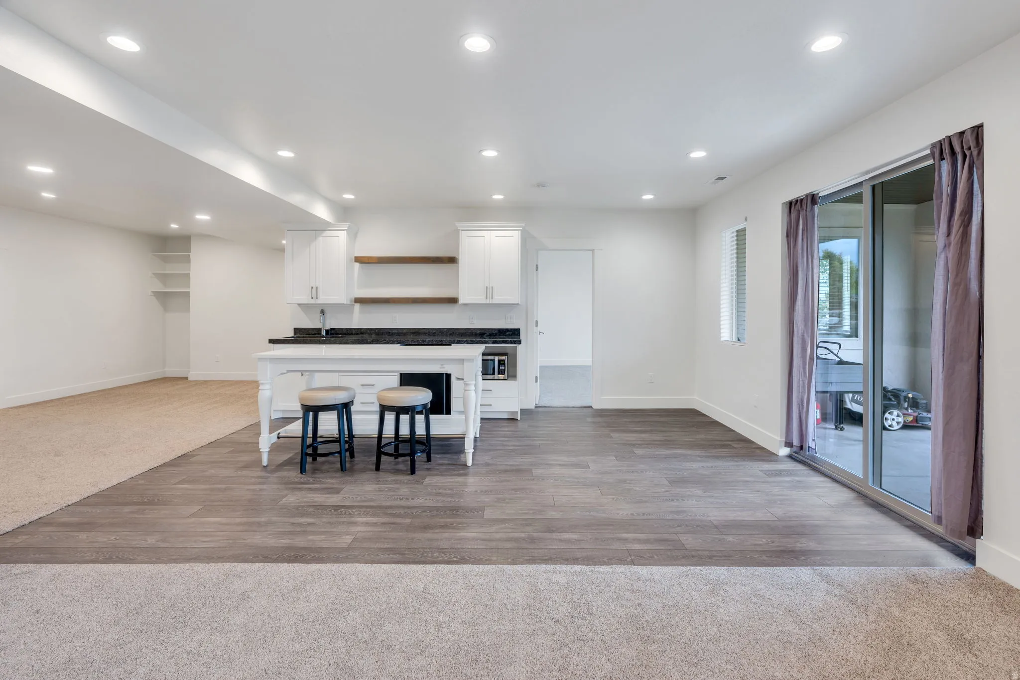 Open-concept living area featuring wood-finish flooring, recessed lighting, and a built-in kitchen with white cabinetry and dark countertops