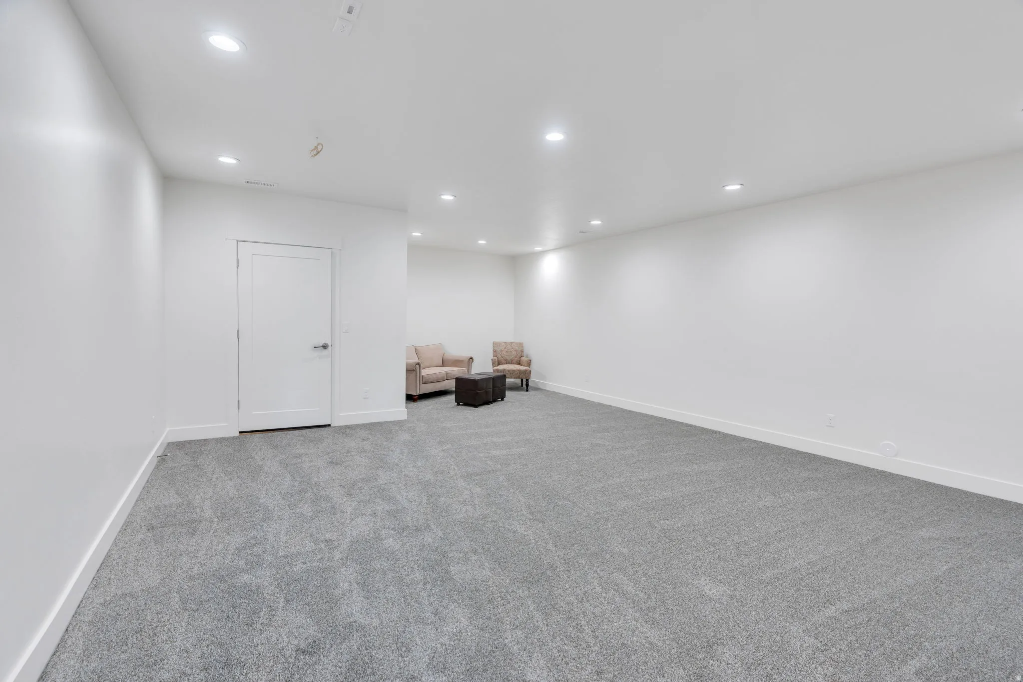 Spacious room featuring neutral carpeting, recessed lighting, and a white interior door