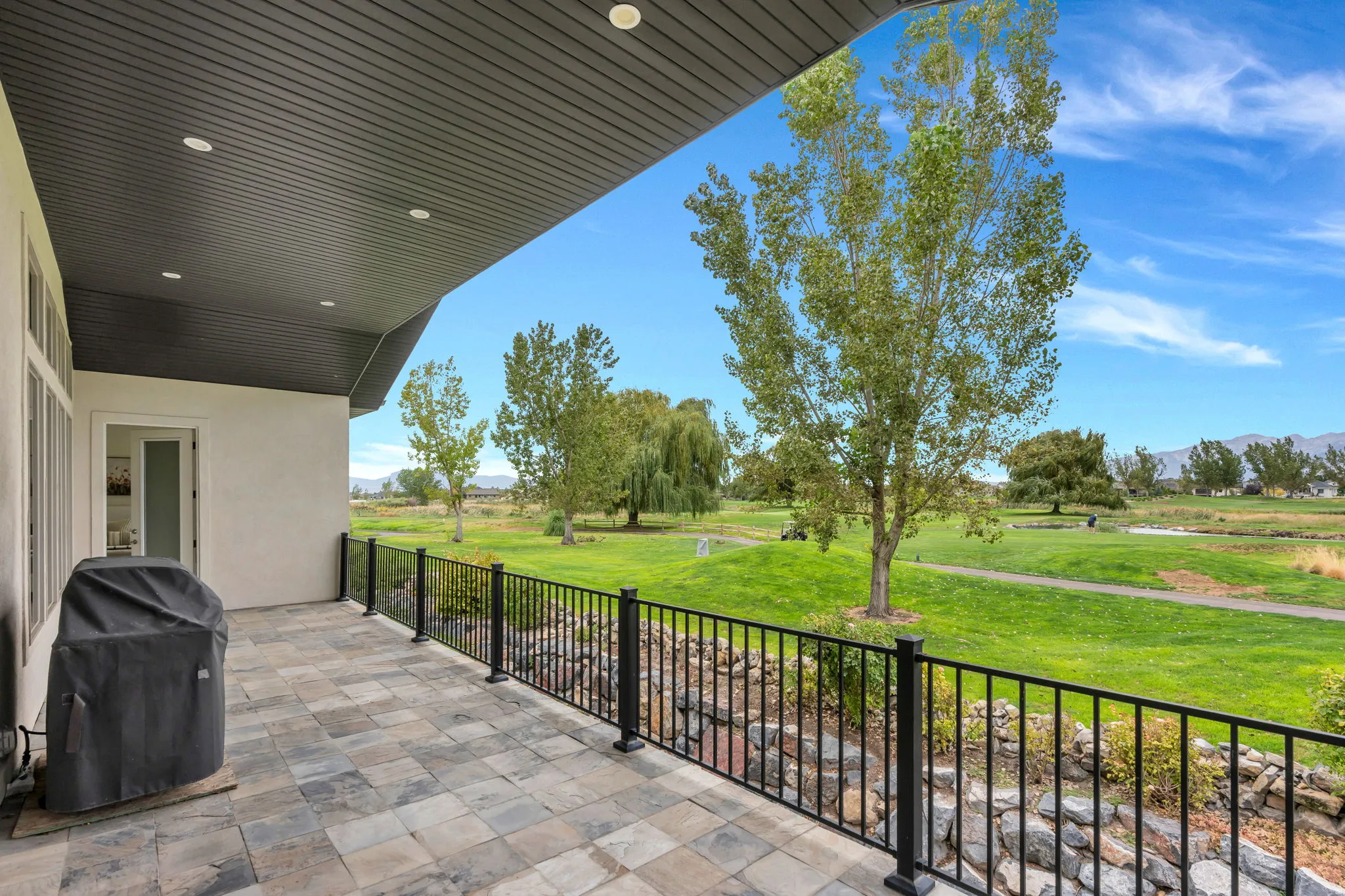 Expansive patio featuring stone pavers, a covered ceiling with recessed lighting, and a metal railing