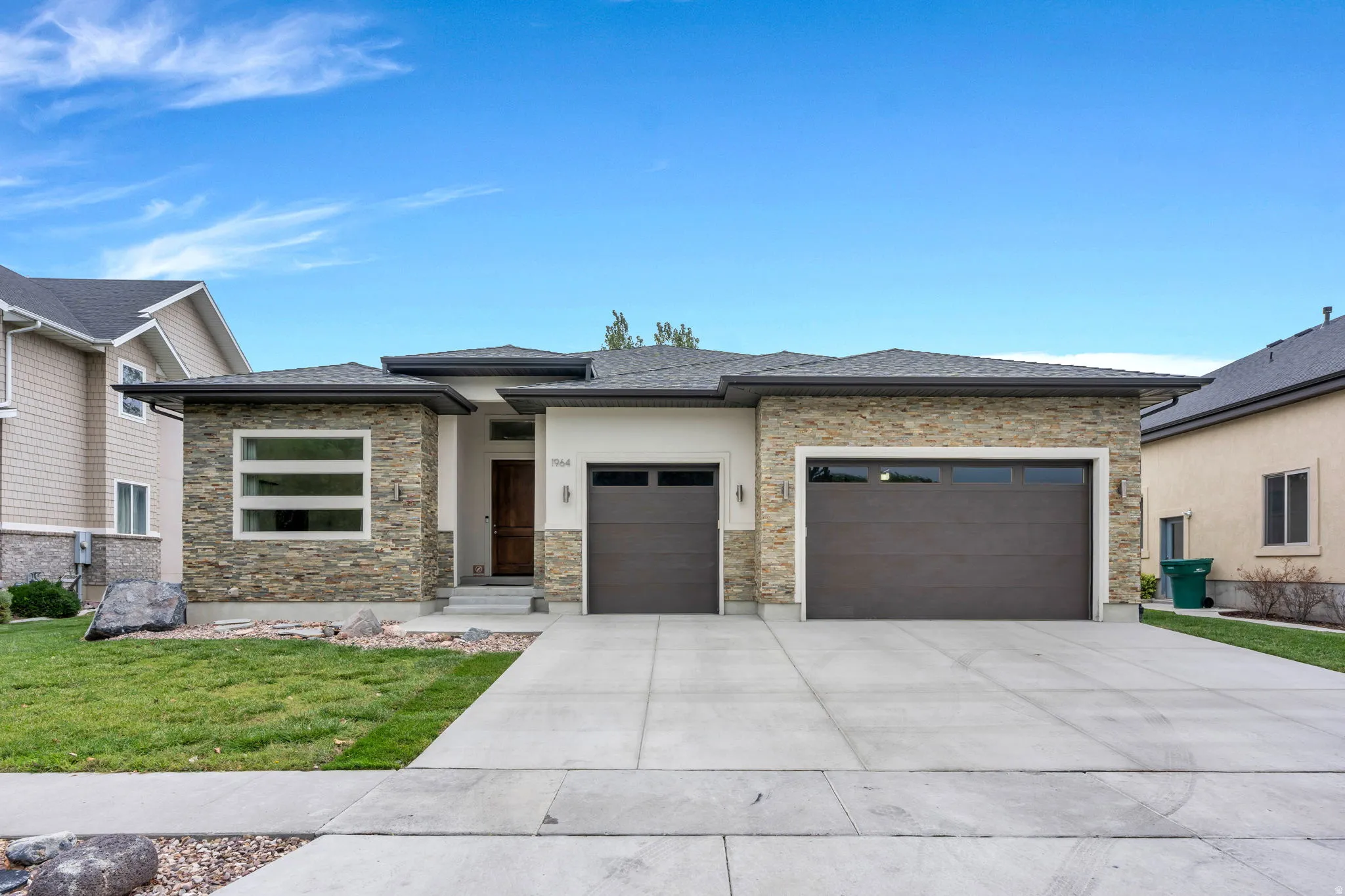Stone veneer exterior with stucco accents, modern horizontal windows, and dual garage doors