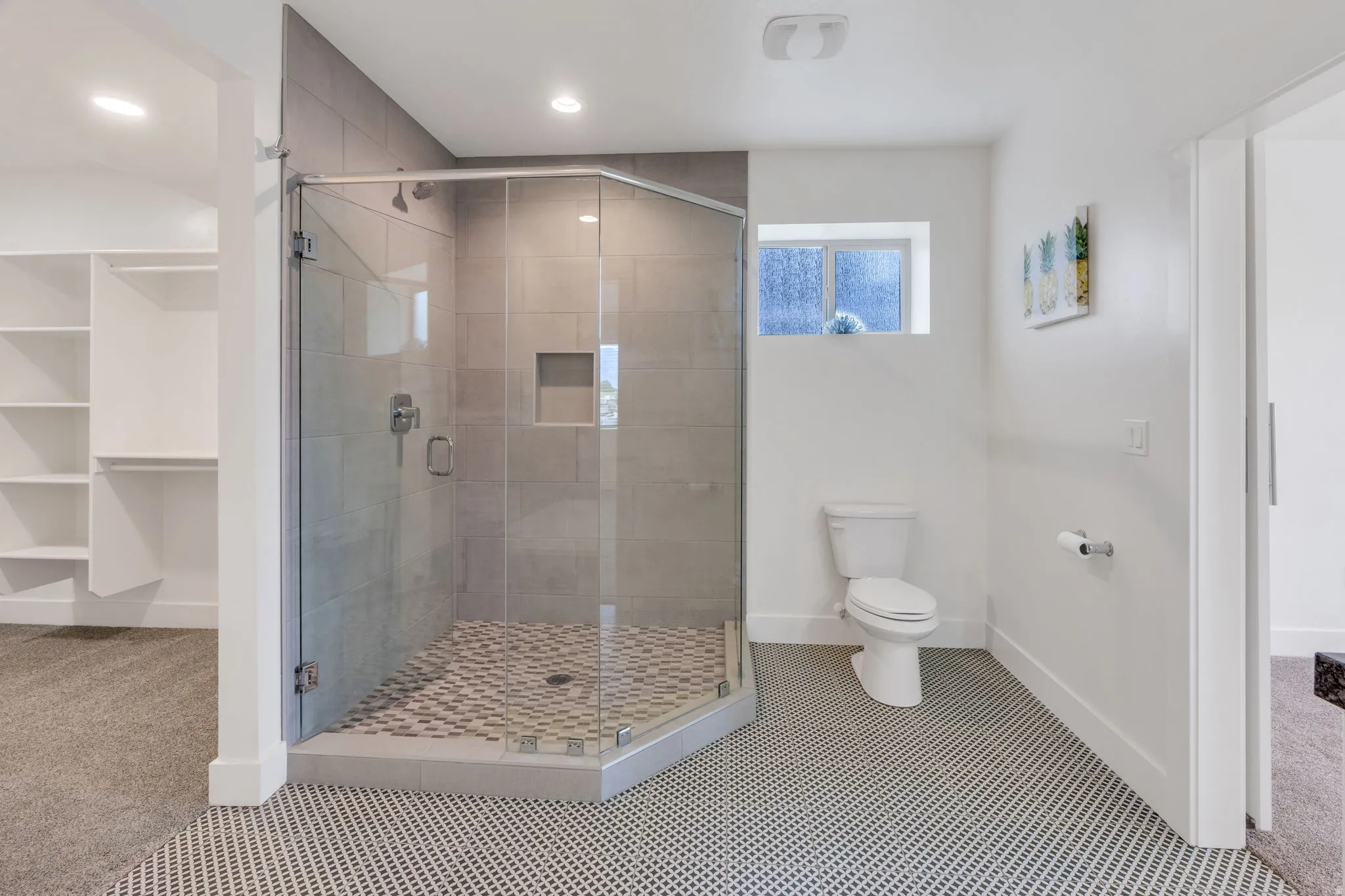 Glass-enclosed shower with tile surround and built-in niche, white toilet, and patterned floor tile